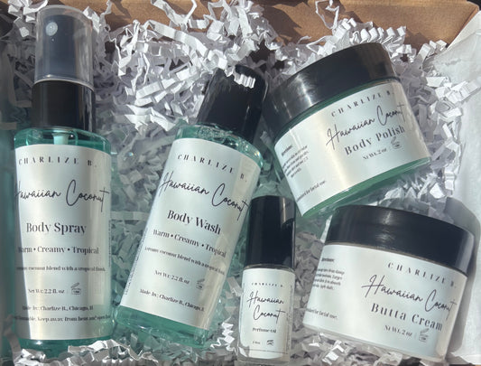 A set of five skincare products from Charelize K Hawaiian Coconut, including body spray, body wash, body polish, butta cream, and a small bottle, arranged in white crinkle paper inside a cardboard box.
